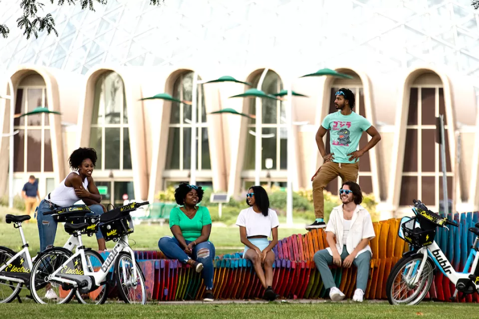 Promotional photo of diverse group of young people sitting on colorful bench with their Bublr bike share e-bikes parked in front of them.